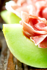 Serrano ham with melon on old wooden table vertical