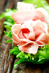 Prosciutto and salad leaves on wooden old table vertical