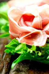 Prosciutto and salad leaves on wooden old table close up