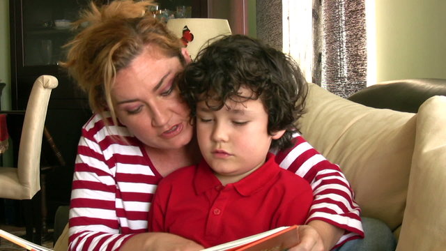 Happy mother and son reading a book sitting on a sofa
