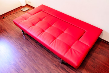 Fototapeta premium An open comfortable red couch on the parquet of a modern apartment 