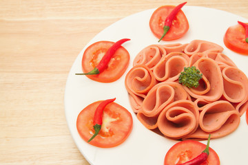 closeup slices of ham on white  plate with tomato and chili