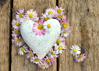 Herz aus Gänseblümchen auf Holzbrett mit Marmorzerz