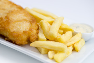 Closeup of battered fish and chips with tartar sauce on white