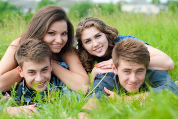 Fototapeta premium Four happy teenage friends lying together on green grass