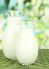 Pitchers of milk on table on bright background