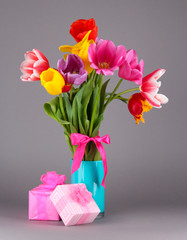 Beautiful tulips in bouquet with gifts on gray background