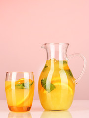 Orange lemonade in pitcher and glass on pink background