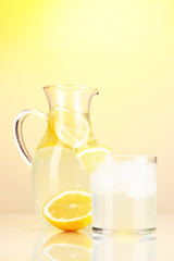 Lemonade in pitcher and glass on yellow background