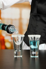 Barmen hand with bottle  pouring beverage into glasses,