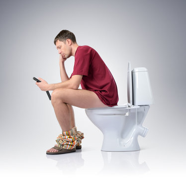 Man with mobile phone sitting on the toilet