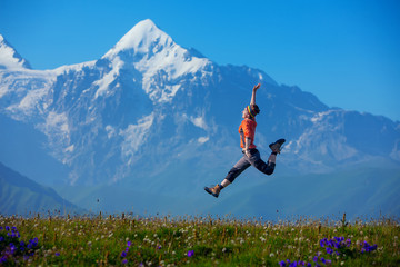 Hikier jumps on meadow against big Caucasus mountains