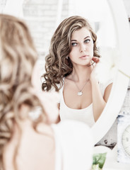 Young beautiful woman looking at her face in the mirror