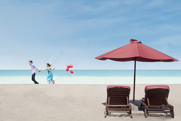 Beautiful couple run near beach chairs and umbrella