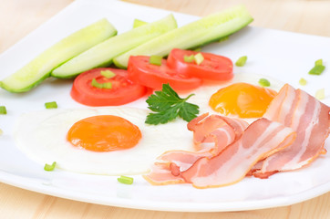 Breakfast with bacon, fried eggs and slices tomatoes