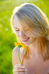 Blond girl take a smell at a flower, smiling