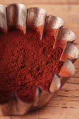 cocoa beans in sieve with cocoa powder in tinware on wood backg