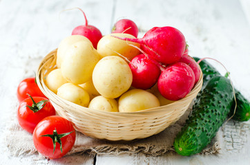 Fresh young potatoes , radish and cucumbers in a basket