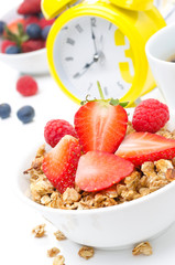 Granola with fresh berries, coffee and yellow alarm clock