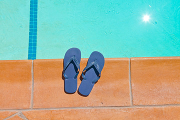 Naklejka premium One pair of blue slippers on the edge of swimming pool.