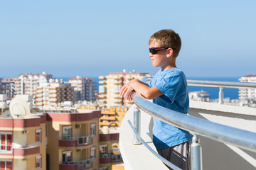 Fototapeta na wymiar A boy stands on balcony of hotel and looks into distance
