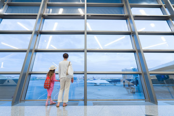 Mother and daughter looking out window at airport terminal
