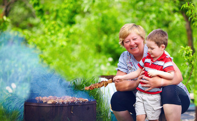 happy grandmother with grandchild roasting meat on picnic