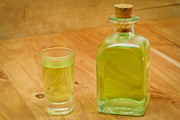 Peppermint liqueur bottle and shot on wooden background