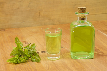 Peppermint plant, liqueur bottle and shot on wooden background