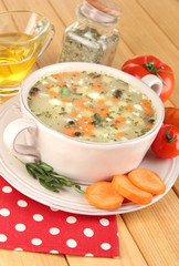 Nourishing soup in pink pan on wooden table close-up