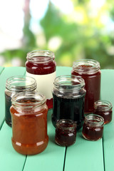 Tasty jam in banks on table on bright background