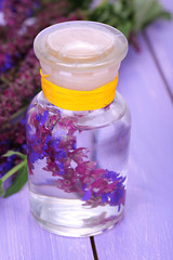 Medicine bottle with salvia flowers on purple wooden background