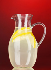 Lemonade in pitcher on red background