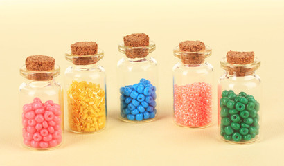 Different colorful beads in bottles on beige background