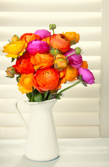 Flowers in a vase with sun light coming out of window blinds