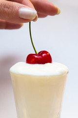 mano che immerge una ciliegia nello yogurt bianco