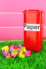 Recycling bin with papers on grass on pink background