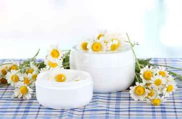 Cream with chamomile on checkered cloth on room background