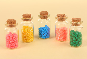 Different colorful beads in bottles on beige background