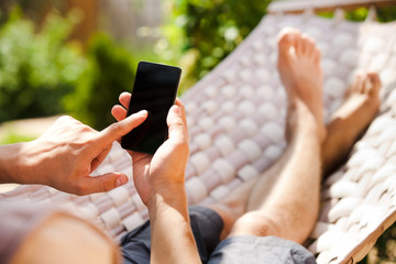 Man using mobile smart phone while relaxing in a hammock