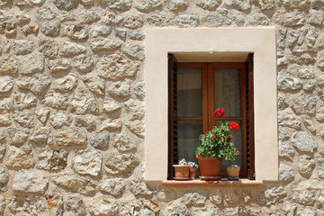 Fototapeta na wymiar Window with flower pots on the stone building wall