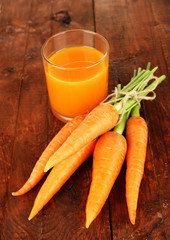 Heap of carrots, glass of juice, on wooden background