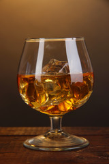 Brandy glass with ice on wooden table on brown background