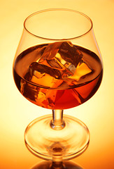 Brandy glass with ice on yellow background