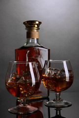 Brandy glass with ice and bottle on grey background