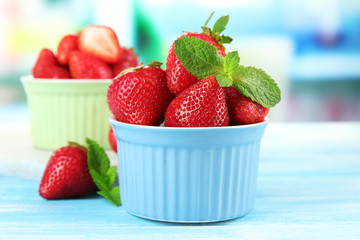 Ripe sweet strawberries in bowls on blue wooden table