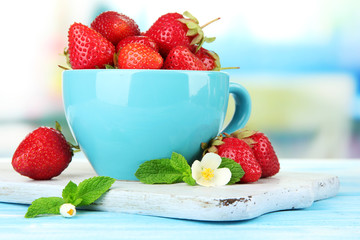 Ripe sweet strawberries in cup on blue wooden table