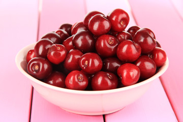 Cherry berries in bowl on wooden table close-up
