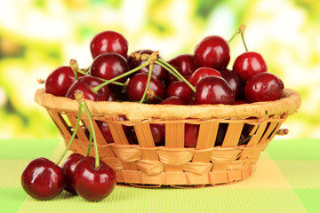 Cherry berries in wicker basket on table on bright background