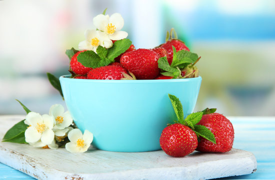 Ripe sweet strawberries in bowl on blue wooden table